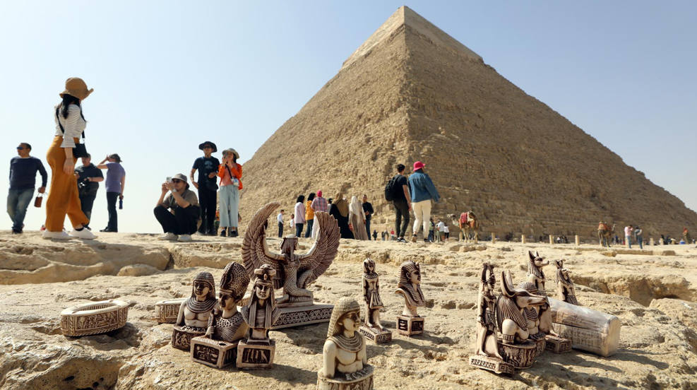 Pequeñas figuritas "souvenirs" descansan en el suelo junto a las pirámides de la meseta de Guiza, ante los ojos de decenas de turistas, que visitan las inmediaciones de El Cairo (Egipto). El Ministerio de Antigüedades de Egipto y el equipo del proyecto Scan Pyramids anunciaron que descubrieron la presencia de un corredor en la pirámide de Keops (Khufu), que podría conducir a la cámara funeraria del faraón, hasta ahora un misterio, ya que aún no se ha encontrado su persona momificada. 