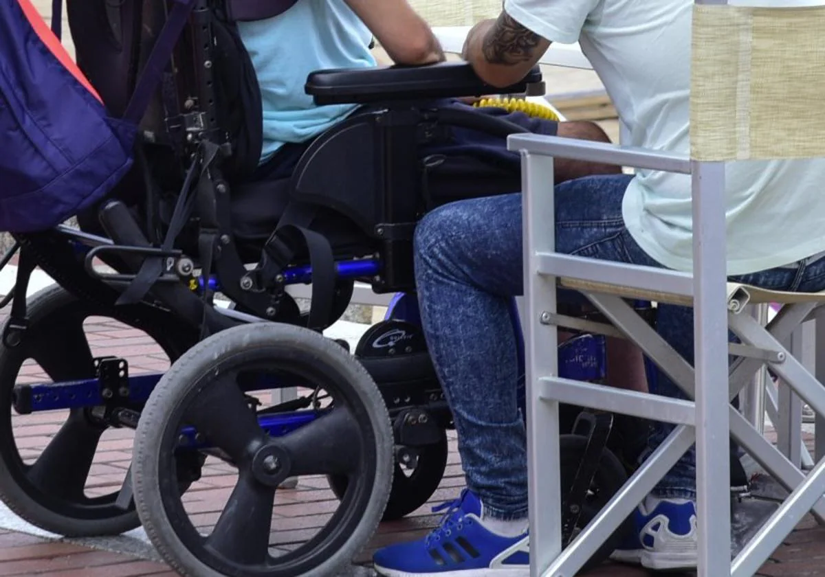 Imagen de archivo de una persona dependiente en silla de ruedas junto a su cuidador.