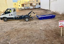 Un vehículo municipal retira escombros de un solar de la capital, con un cartel de recordatorio.