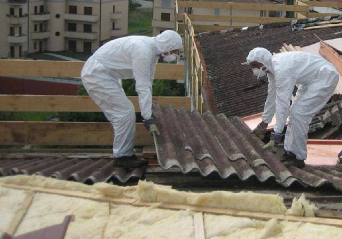 Dos trabajadores retirán planchas de amianto de la cubierta de un edificio.
