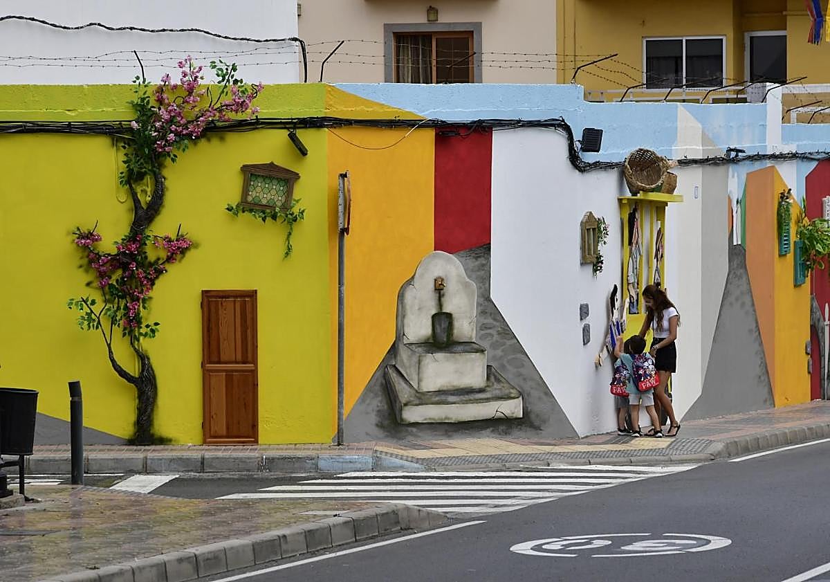 Imagen principal - En la foto superior, espectacular mural junto al que pasará la romería. Debajo, una vecina posa con la Vara de la Romera, y una de las cruces engalanadas que estos días luce El Tablero.