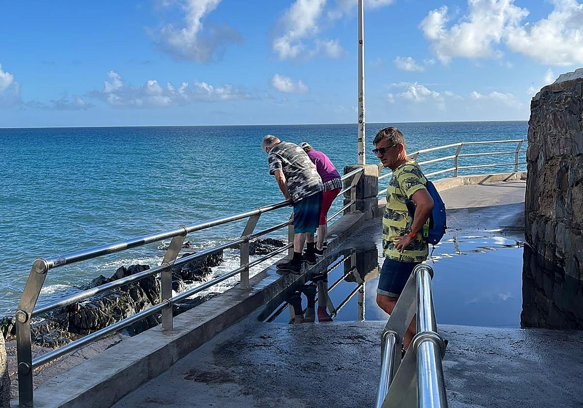 Turistas, esta tarde, alongados en la barandilla del paseo para sortear los charcos