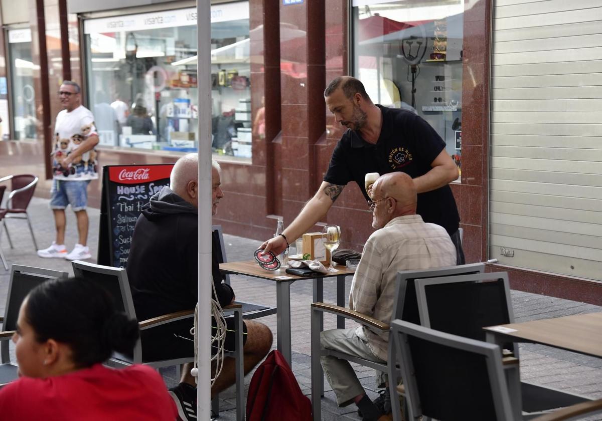 Un camarero sirve a dos clientes en una terraza de la capital grancanaria.