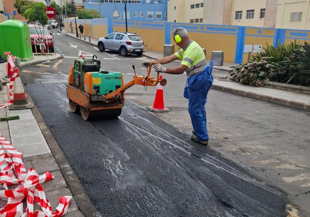 Un operario trabaja en la reparación del asfalta dañado por la quema de contenedores en la calle Drago.