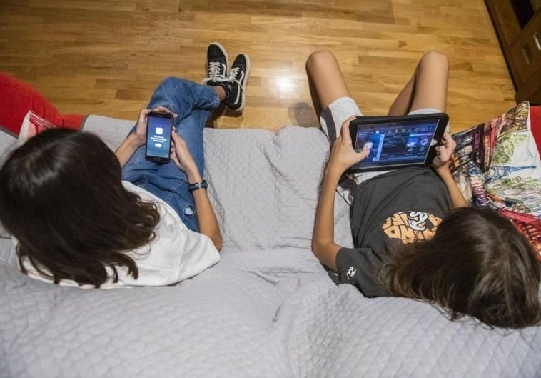 Dos menores se entretienen con las pantallas, el primero con el móvil y el segundo con un videojuego.