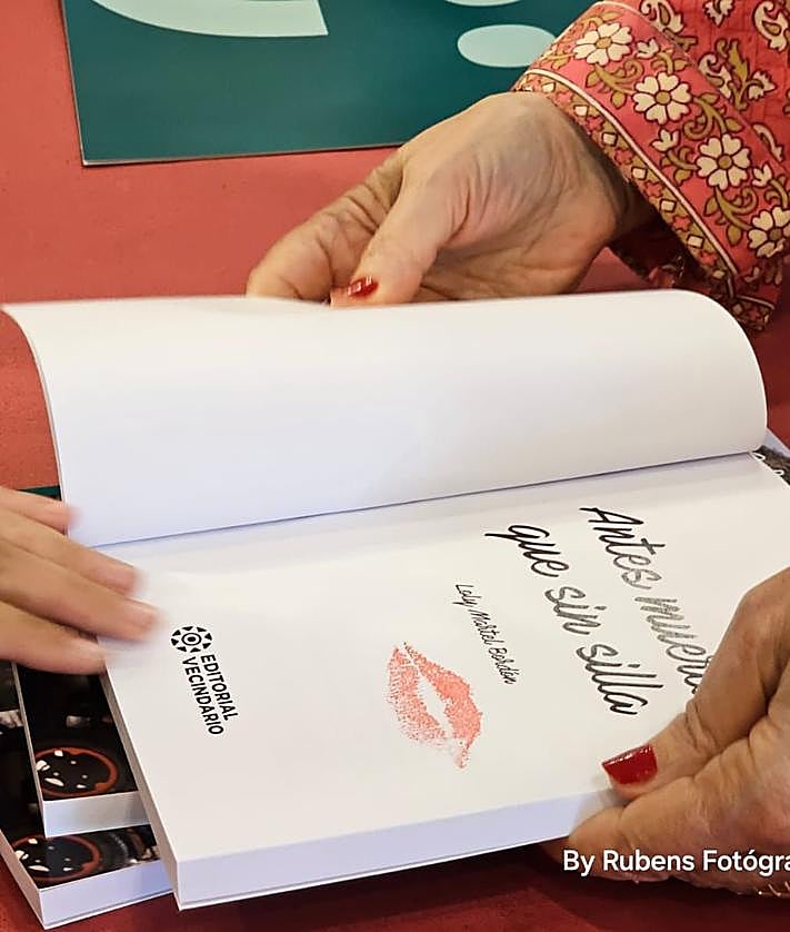 Imagen secundaria 2 - Arriba, Paqui Domínguez ayuda a Loly durante el acto. Debajo, los músicos Germán López y José Artiles. Y libro firmado por un beso de Loly hecho sello.