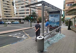 Los usuarios de guaguas esperan sobre los cristales de la marquesina rota.