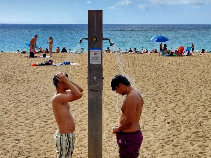 Dos jóvenes, en las duchas de la playa de Las Canteras este lunes.