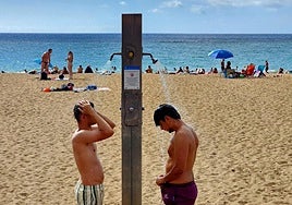 Dos jóvenes, en las duchas de la playa de Las Canteras este lunes.