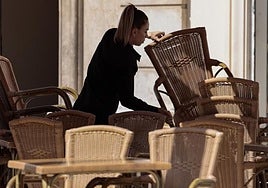 Una camarera apila las sillas en la terraza de un restaurante.