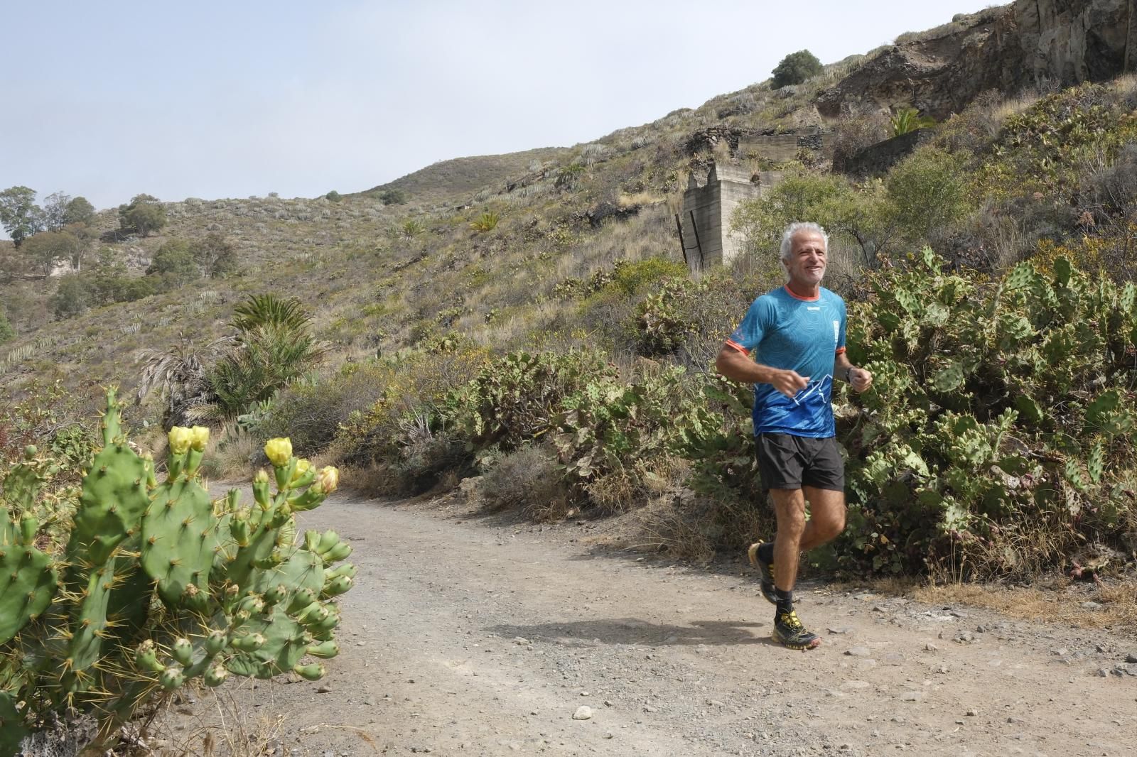Imagen principal - Arriba, Casimiro Martín disfruta de los senderos y barrancos para ir a correr. Abajo a la izquierda, La GC-308, carretera principal que transcurre por todo el pueblo. A la derecha, José García, en la plaza.