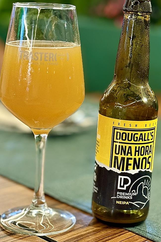 Copa llena de la cerveza «Una Hora Menos» junto a un botellín.