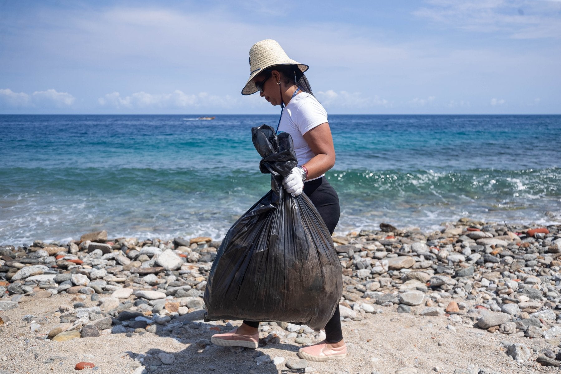 Una mujer con una bolsa de basura recogida en una playa.