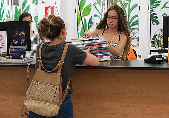 Foto de archivo de una mujer comprando un lote de libros de texto para la vuelta al cole.