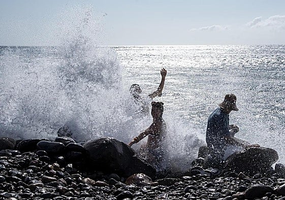 Varias personas se refrescan con la espuma de las olas rompiendo en La Aldea.