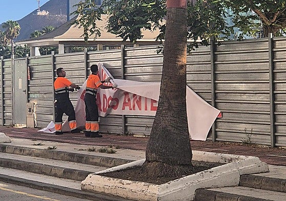 Operarios municipales retiran una de la pancarta que se colocó en el vallado de la obra.