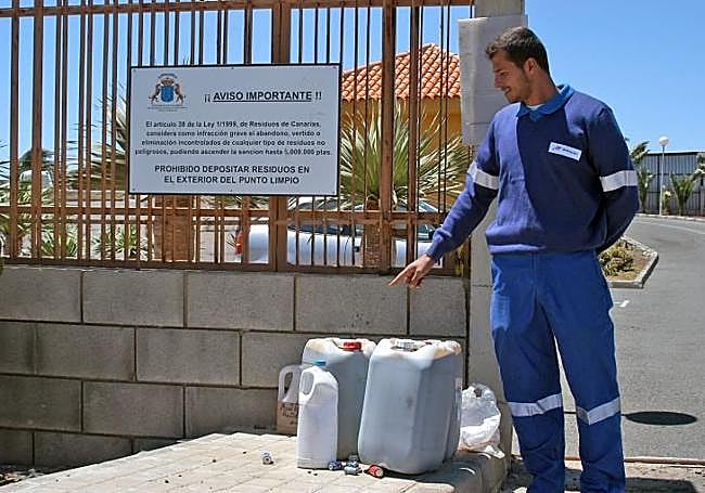 Un operario señala garrafas de aceite dejadas en la puerta de un punto limpio.