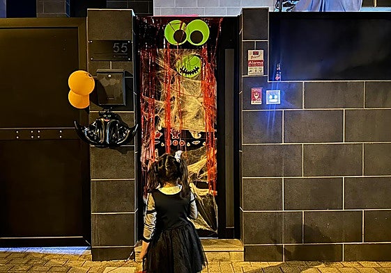 Imagen de una niña tocando en una casa decorada con temática Halloween.
