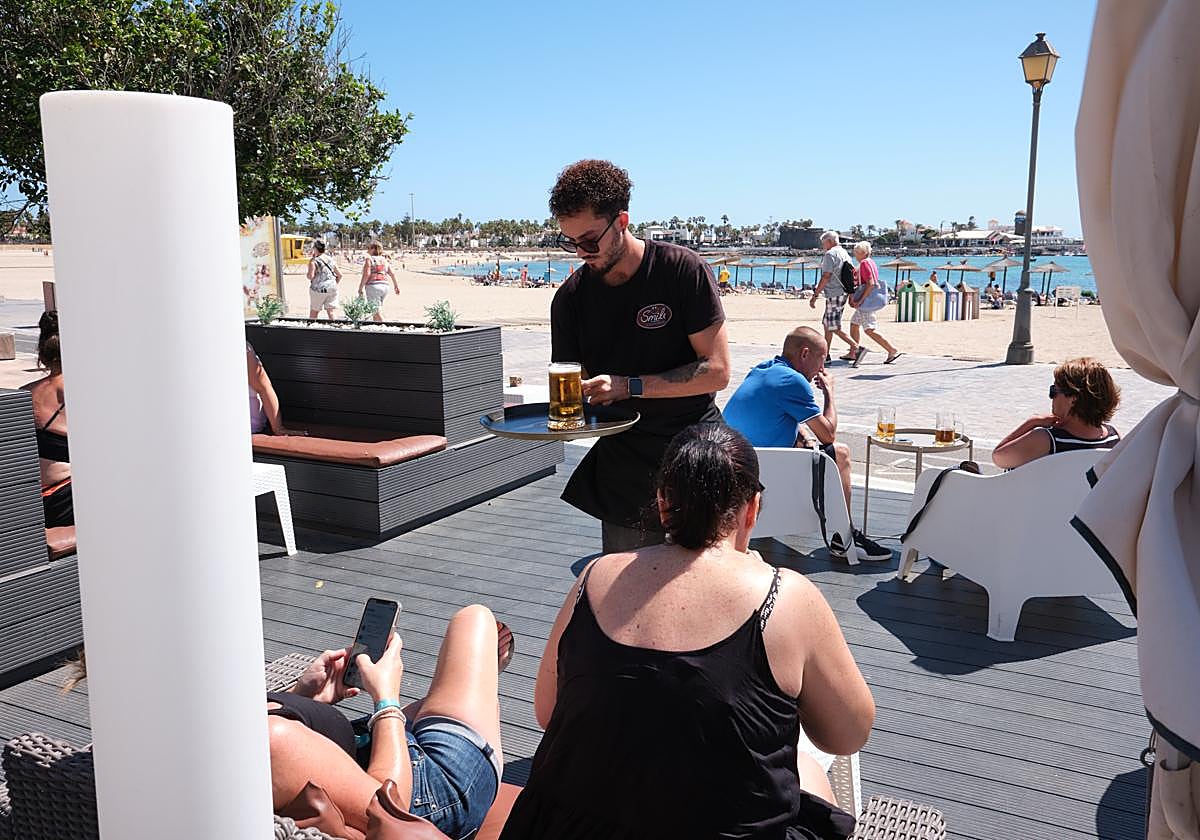Camarero atiende a los clientes en una terraza de la playa de El Castillo, en el municipio de Antigua.