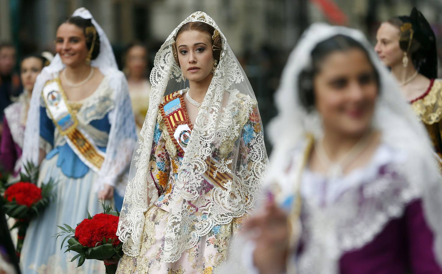 Varias falleras se dirigen a la plaza de la Virgen de los Desamparados para depositar sus ramos de claveles rojos