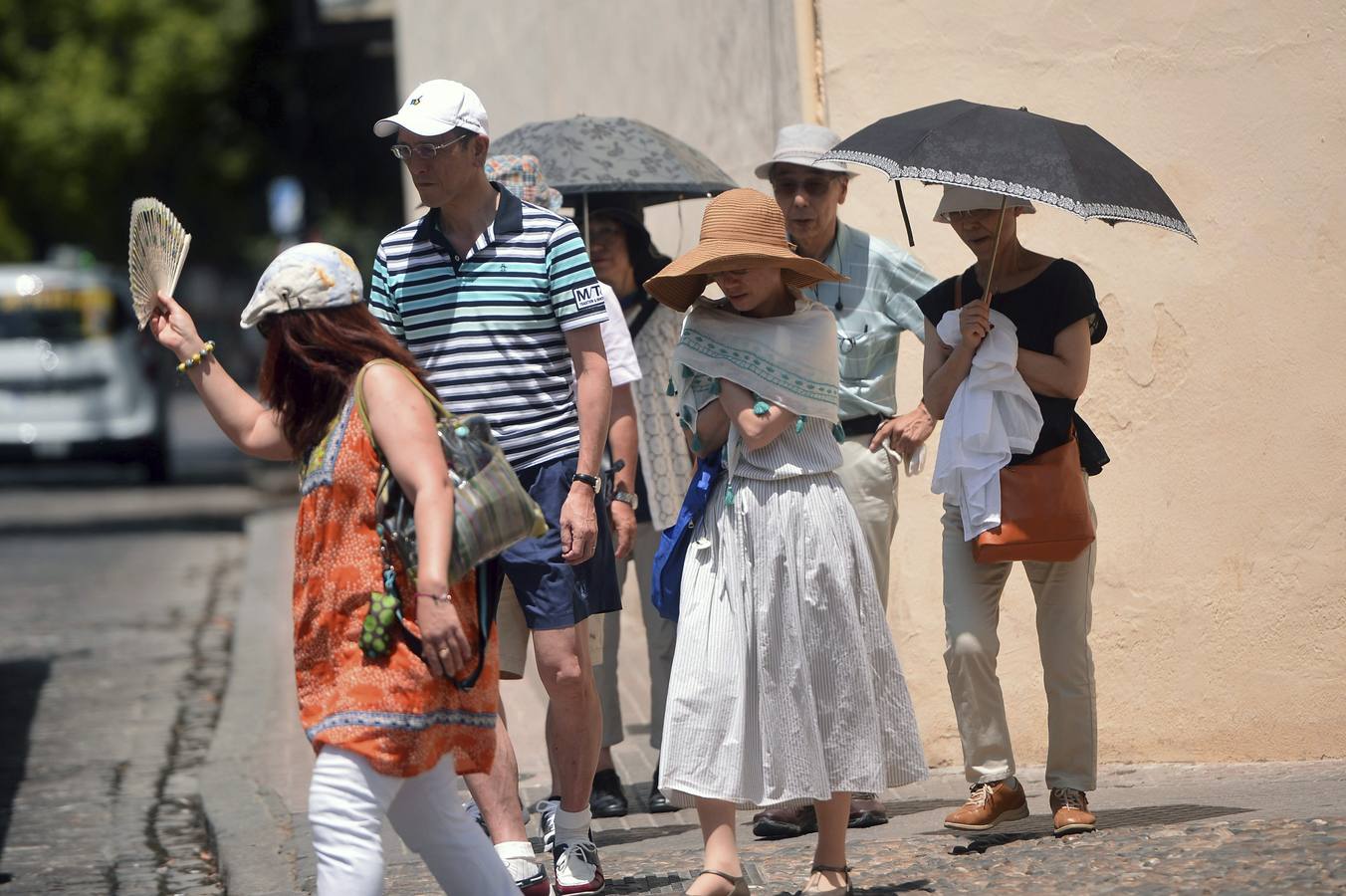 Un grupo de turistas se tapan con sombrillas y pañuelos para seguir su visita por Córdoba.