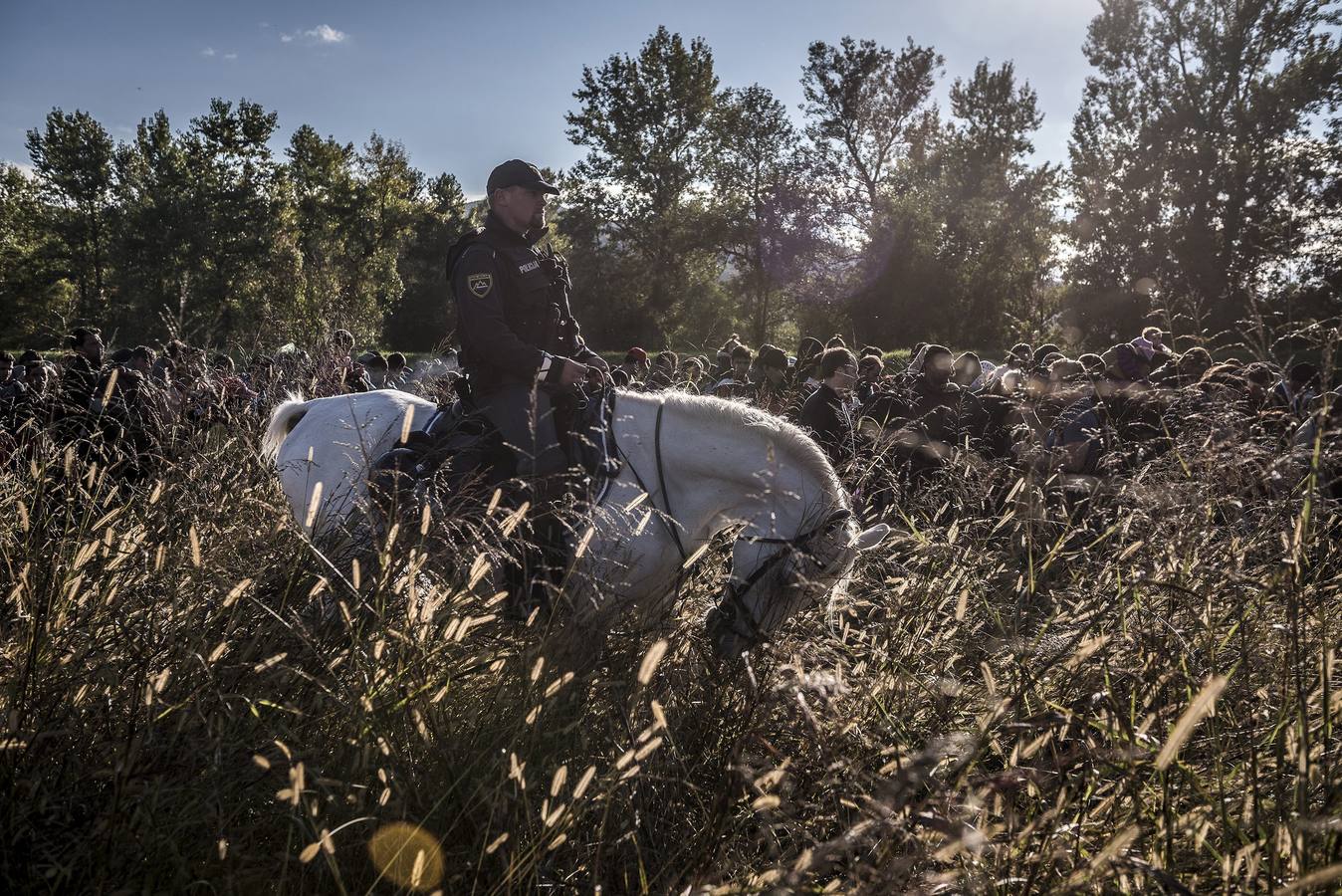 Fotografía de la serie ganadores de noticias de actualidad. La fotografía muestra un grupo de migrantes caminando encima de un dique mientras la policía antidisturbios eslovena los acompaña al campo de registro de Dobova (Eslovenia).