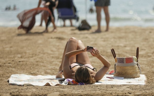 Una mujer consulta el móvil mientras trata de disfrutar de la playa. :: MANUEL BRUQUE / efe