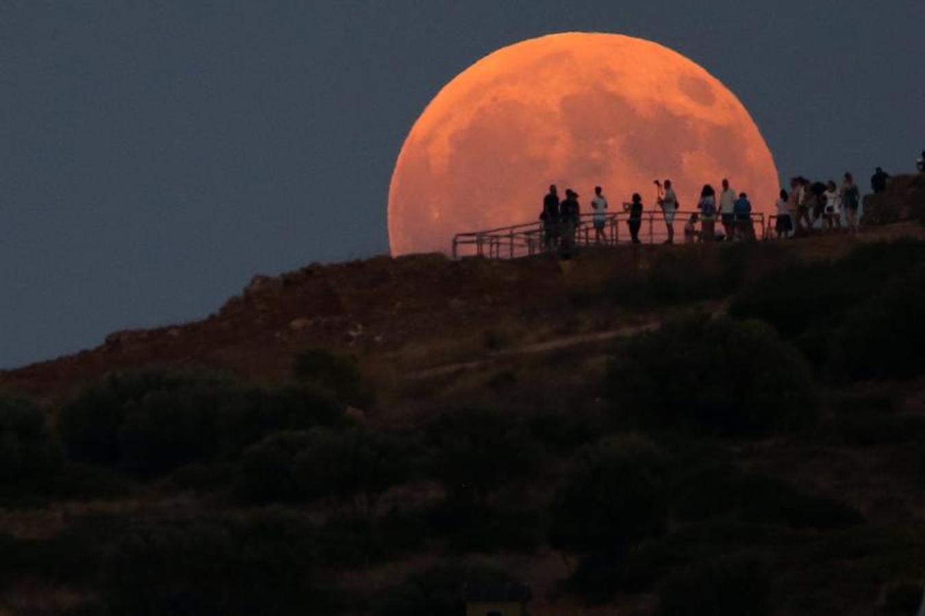 Personas admiran la luna llena que se levanta sobre el templo de Poseidón .