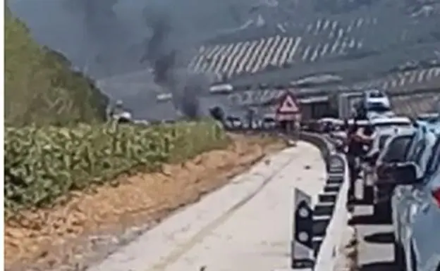 Imagen del coche incendiado y de las retenciones registradas en Las Pedrizas.