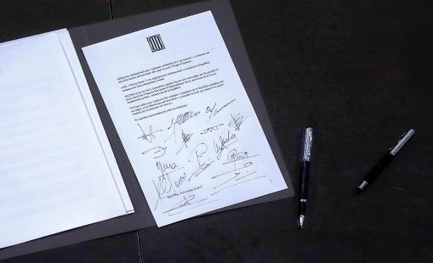 El presidente de la Generalitat, Carles Puigdemont, firma el documento. Arriba, el contenido del texto. :: martín benet / reuters
