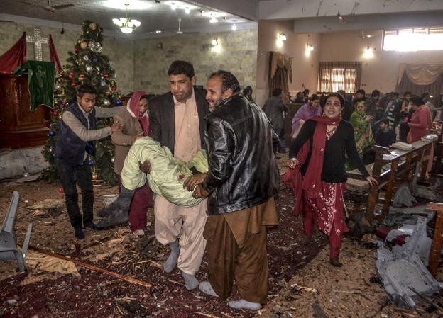 Varios hombres se llevan a heridos tras el atentado durante la celebración de los actos de Navidad dentro del templo de Quetta, en Pakistán. :: A. CALVIN / AFP