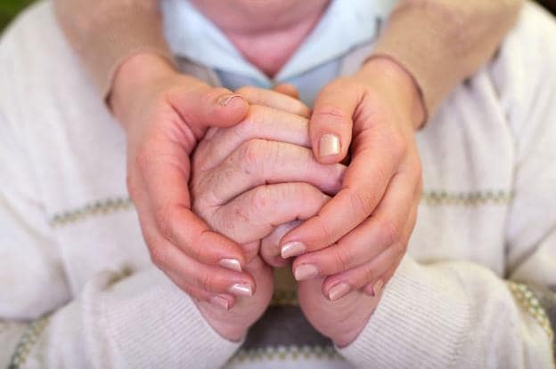 Un cuidador coge las manos de un anciano con una demencia. :: r. c.
