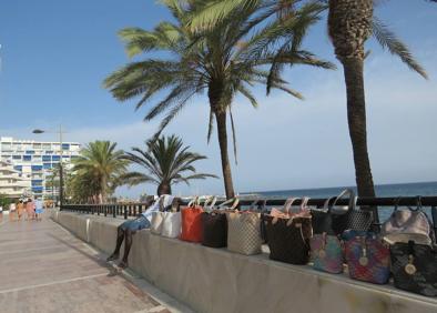 Imagen secundaria 1 - Un turista se interesa por los colgantes. Un mantero vende sus productos en el paseo marítimo de Marbella. También venden comida y bebida en la playa.