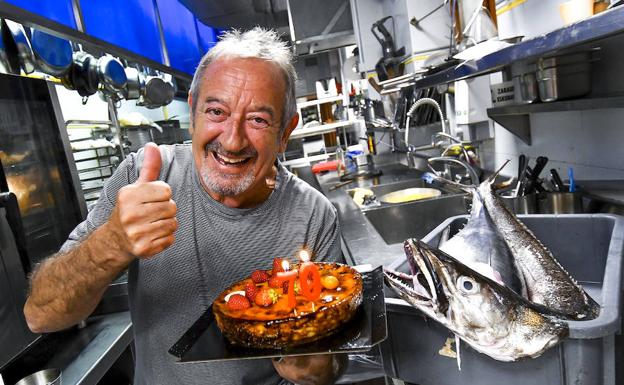 Karlos Arguiñano sujeta una tarta con velas en la cocina de su restaurante ante la atenta mirada de una merluza.