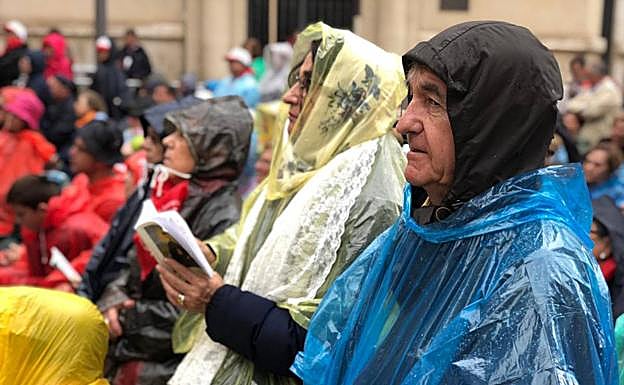 Fieles siguen el acto de beatización desde fuera de la basílica equipados para la lluvia. 