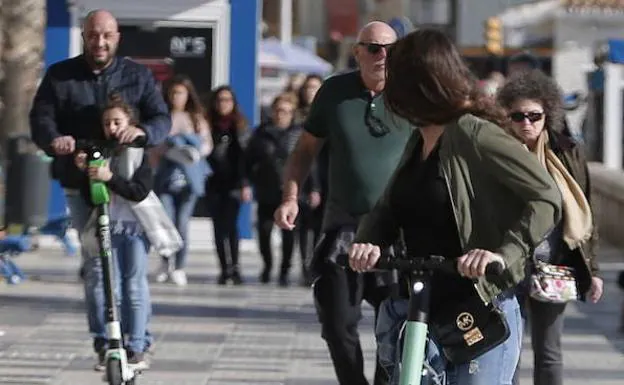 Usuarios a bordo de patinetes de alquiler en el paseo marítimo de la capital.