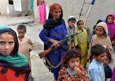 Imagen secundaria 1 - Arriba, algunos de los niños caminando delante de Hamisha Gul, el patriarca. Abajo, a la izquierda, junto a la abuela Niaz Bibi, armada con un fusil. Y a la derecha, la pequeña Marwa, de seis años, que perdió a su madre, su hermana gemela y a dos de sus primos, escribiendo en la rudimentaria pizarra que tienen en casa. 