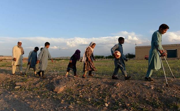 Imagen principal - Arriba, algunos de los niños caminando delante de Hamisha Gul, el patriarca. Abajo, a la izquierda, junto a la abuela Niaz Bibi, armada con un fusil. Y a la derecha, la pequeña Marwa, de seis años, que perdió a su madre, su hermana gemela y a dos de sus primos, escribiendo en la rudimentaria pizarra que tienen en casa. 