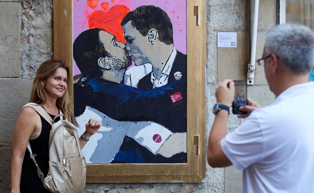 Una persona posa junto a un moral que representa a Pablo Iglesias y Pedro Sánchez besándose. 