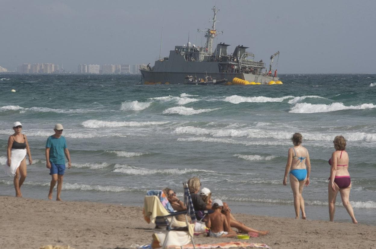 Bañistas pasean por La Manga frente al cazaminas 'Turia', después de que embarrancara. :: a. gil / agm