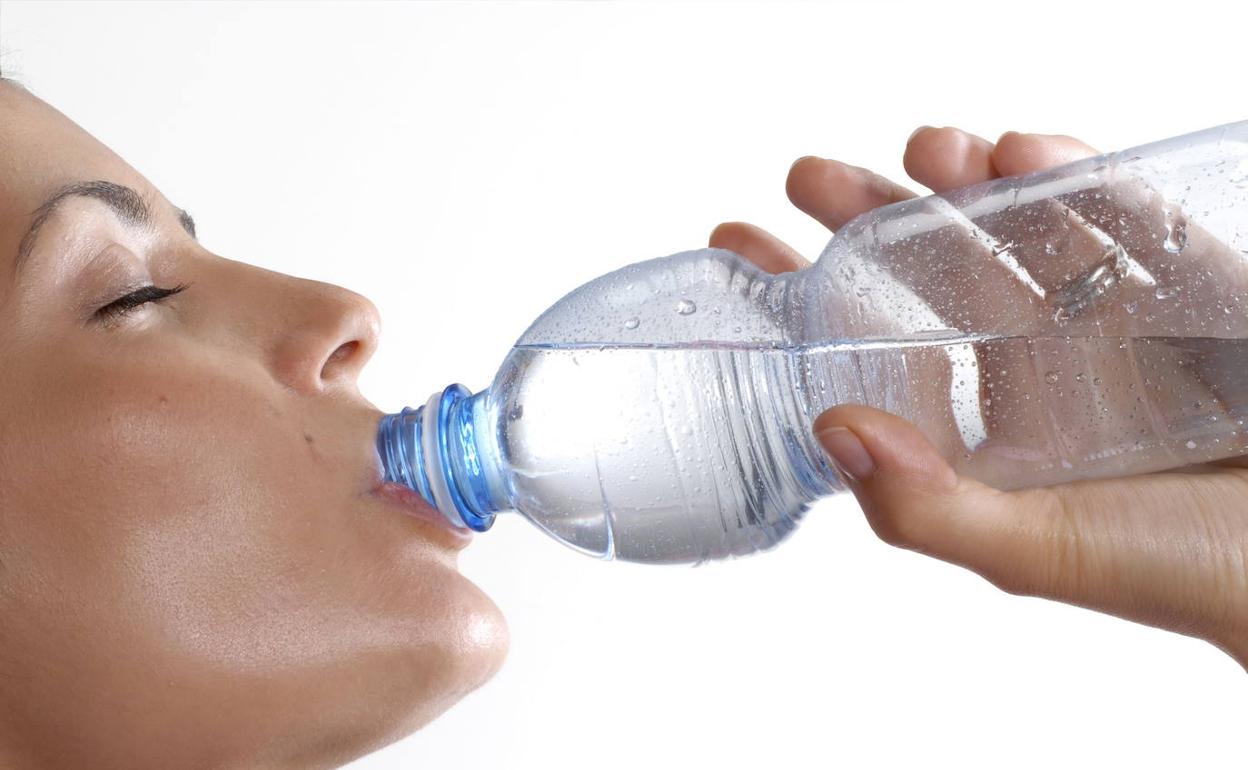 Una mujer bebe agua de una botella. 