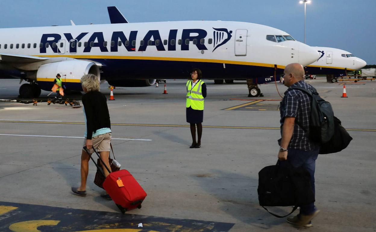 Imagen de archivo de dos pasajeros con equipajes de mano junto a un avión de Ryanair. 