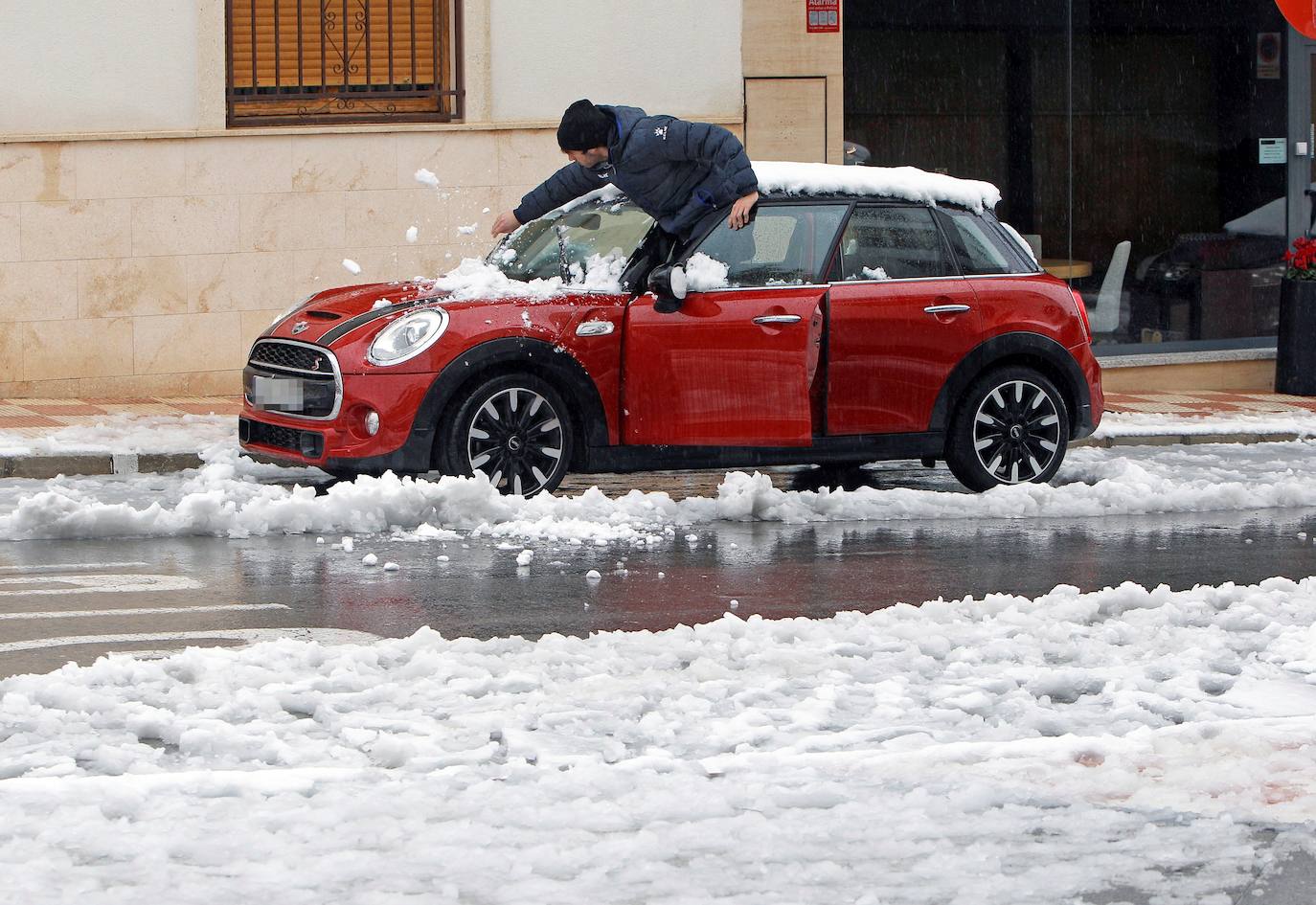 Un hombre limpia su vehículo de nieve en la localidad alicantina de Castalla