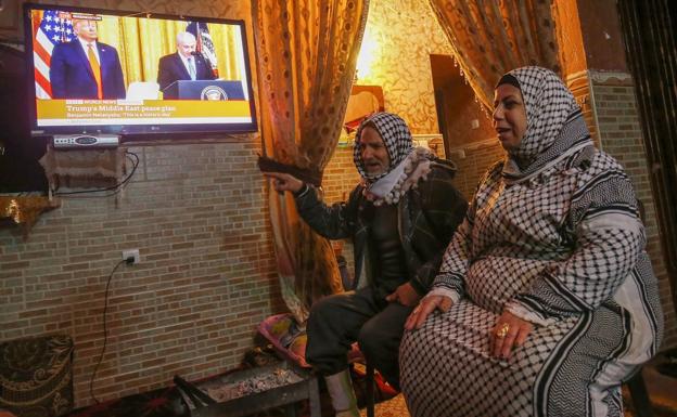 Dos mujeres palestinas siguen por televisión la presentación del plan de paz de Trump.