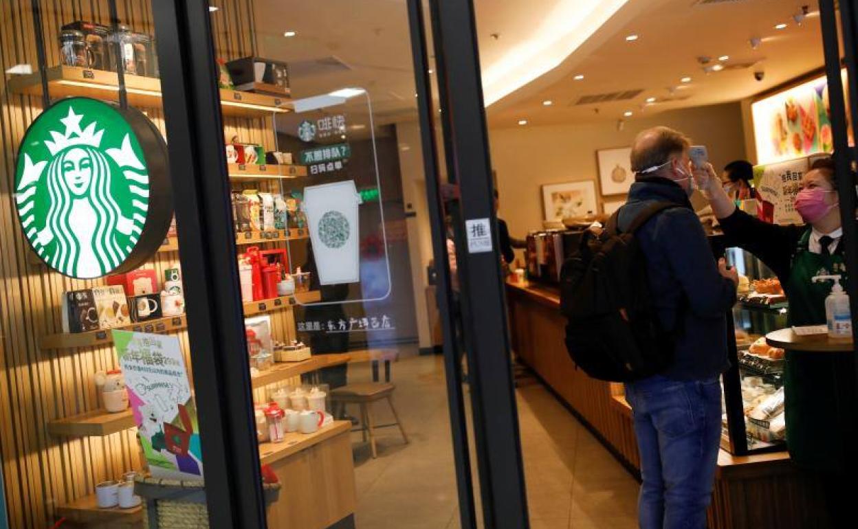 Un trabajador utiliza un termómetro para verificar la temperatura de un cliente al entrar a una tienda de Starbucks en Pekín.