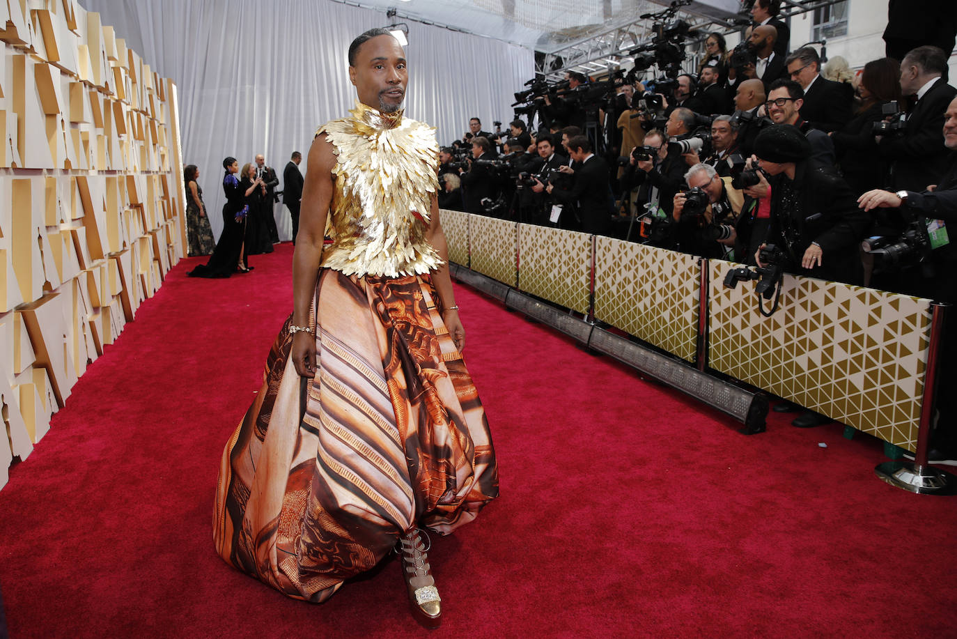 Billy Porter firmó uno de los looks más surrealistas y estrafalarios de esta alfombra roja. Tanto que incluso la cuenta oficial en Twitter de la Academia lo compartió. El diseño en sí se llama Cupola y, como él mismo ha desvelado en sus redes sociales, es un modelo de costura hecho a medida por el inglés Giles Deacon. Lleva un top de plumas doradas sin mangas y una enorme falda abullonada en tonos tierra con un print inspirado en el palacio de londinense Kensignton, actual residencia de los duques de Cambridge. Sandra Choi, directora creativa de Jimmy Choo, creó para él además unas suntuosas botas doradas con plataforma que son todo un homenaje a la cultura drag que Porter reivindica en cada aparición pública. 