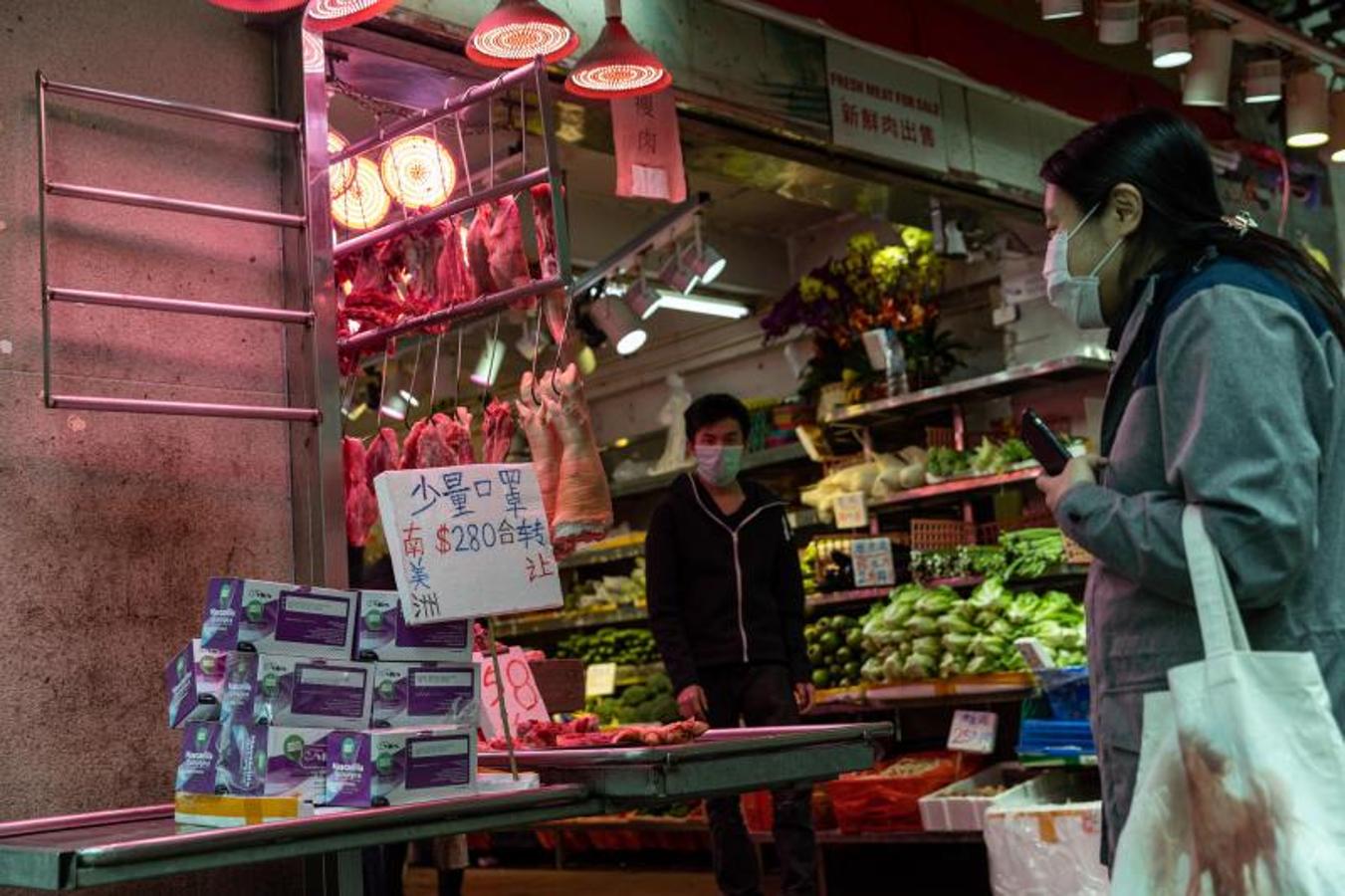 Una mujer mira cajas de máscaras faciales, importadas de América del Sur, para la venta en un puesto de carnicería en Hong Kong
