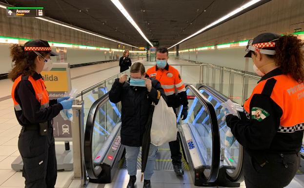 Voluntarios entregan una mascarilla a una usuaria del metro de Málaga, esta mañana. 