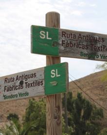 Imagen secundaria 2 - Arriba, señales indicativas de esta ruta. Abajo, a la izquierda, los primeros metros discurren por la acera, y, a la derecha, señales en el punto donde el carril de tierra llega a la carretera.