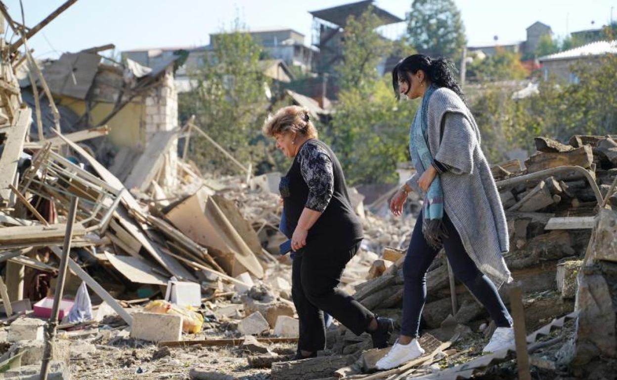 Dos mujeres caminan sobre las ruinas de una casa en la ciudad de Stepanake.